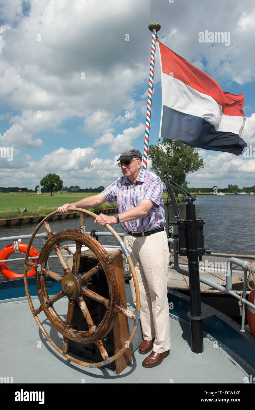 Old man at the helm of a boat with Dutch flag, Amersfoort, Netherlands Stock Photo