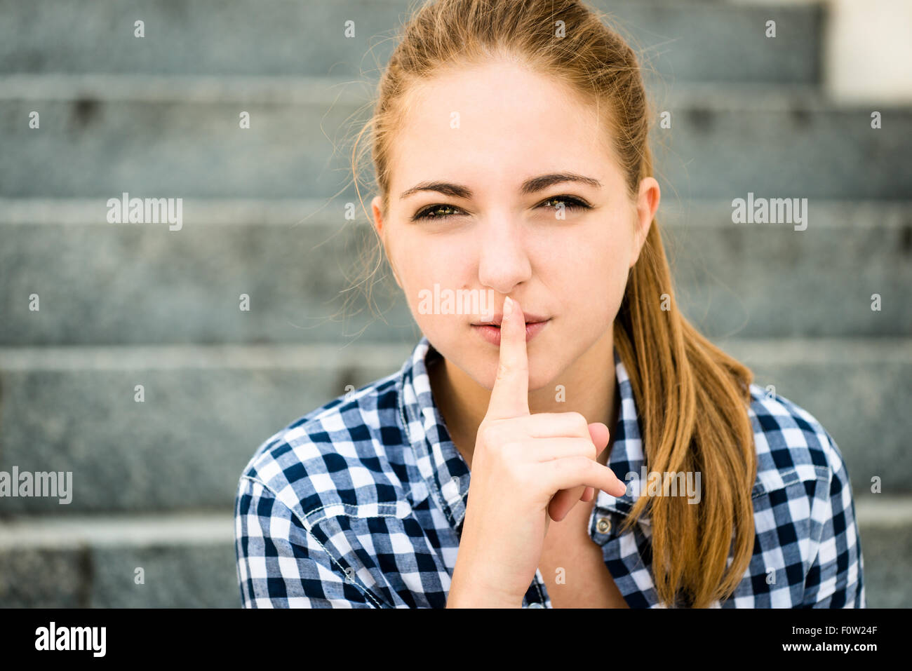 Teenager with finger on mouth as a sign of silence outdoor in street Stock Photo