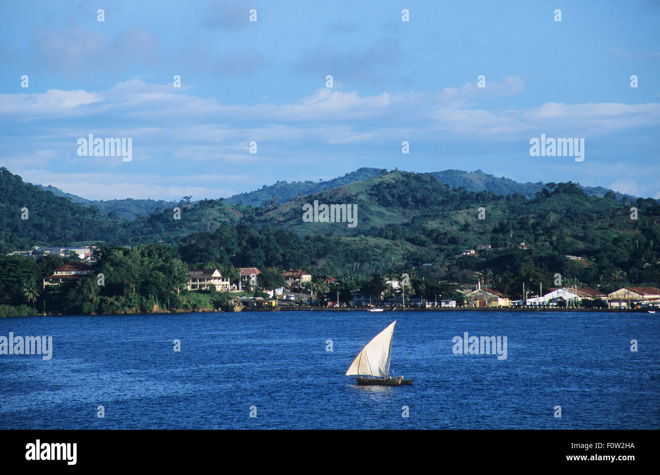 A pirogue sails past Andoany or Hell-Ville's shore, capital of Nosy Be island, where colonial buildings have been restored, Diana Region, Madagascar, Indian Ocean Stock Photo