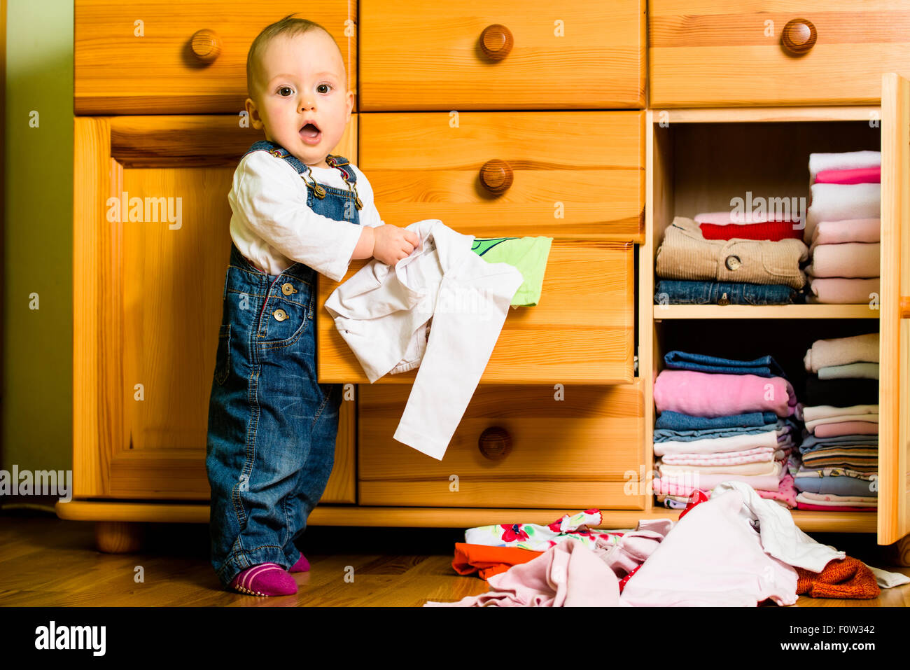 Baby throws out clothes from wooden furniture at home Stock Photo Alamy