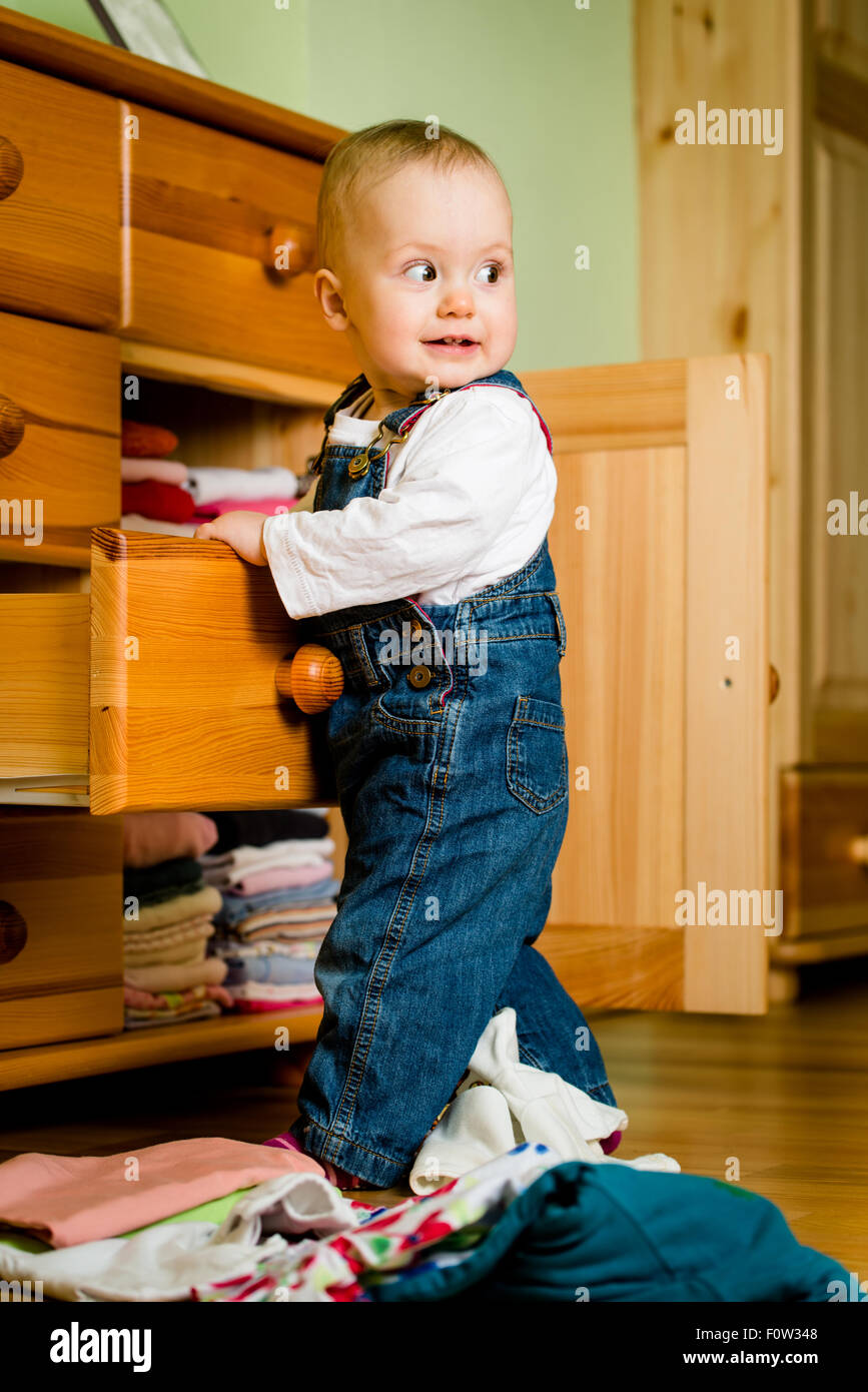 Baby throws out clothes from wooden furniture at home Stock Photo Alamy