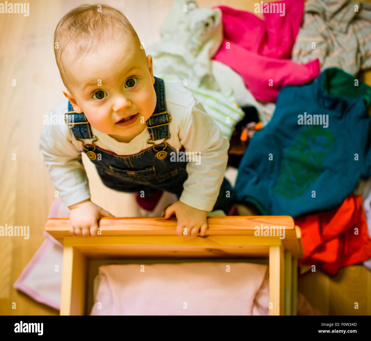 Baby throws out clothes from wooden furniture at home Stock Photo Alamy