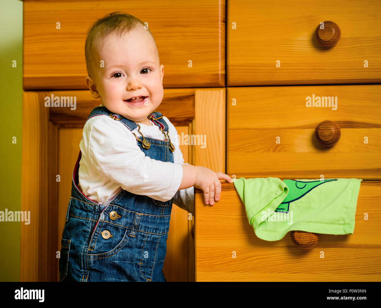 Baby opening drawer with clothes on wooden furniture at home Stock