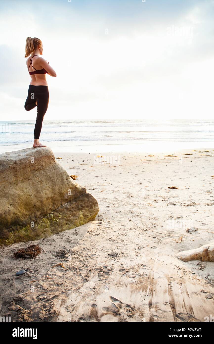 Mid adult woman practicing tree yoga pose on beach rock Stock Photo - Alamy