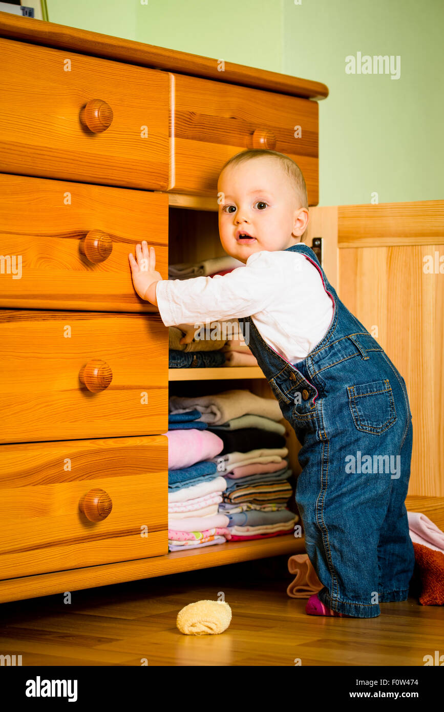 Baby throws out clothes from wooden furniture at home Stock Photo Alamy