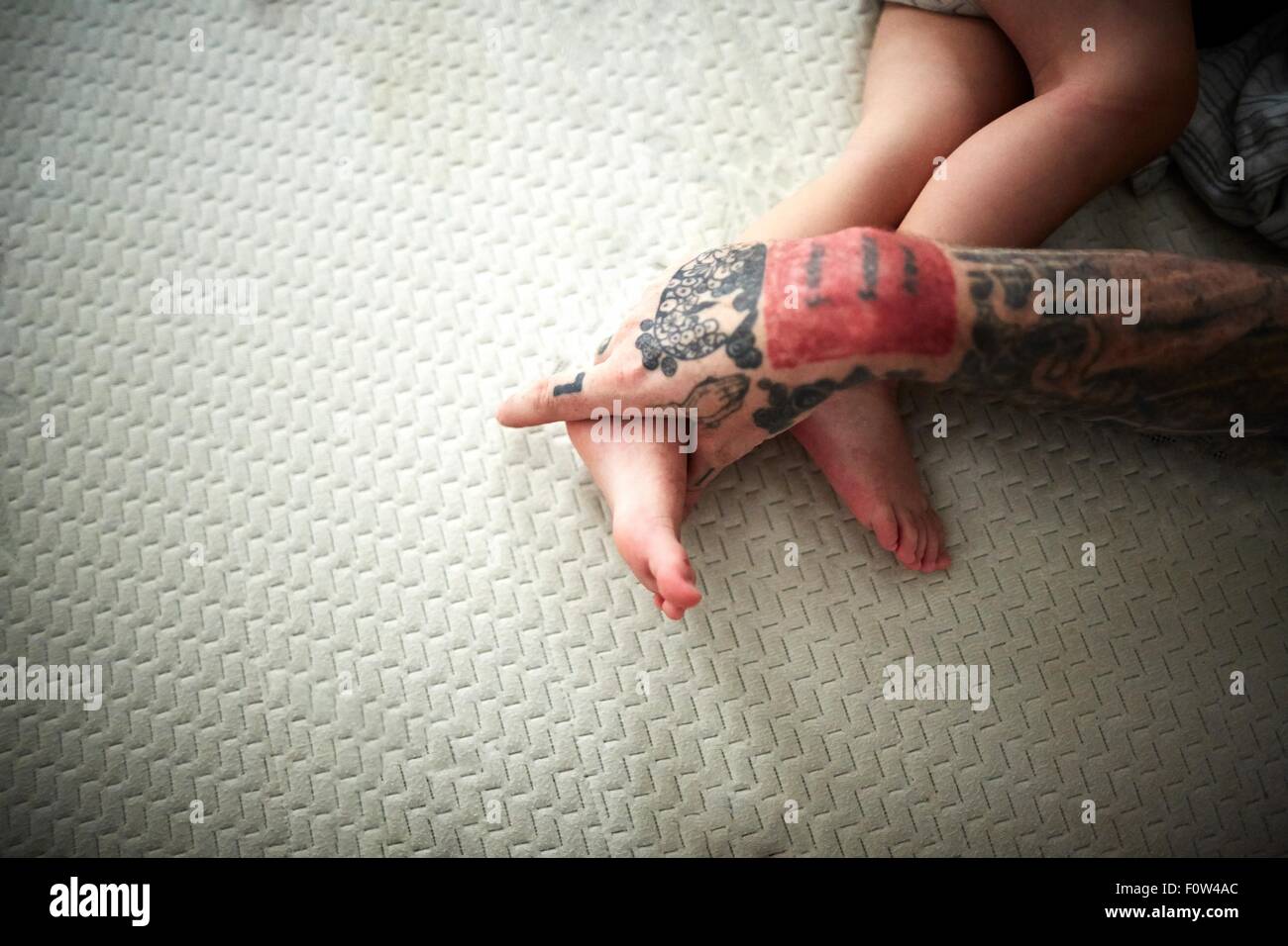 Tattooed hand resting on boy's legs Stock Photo