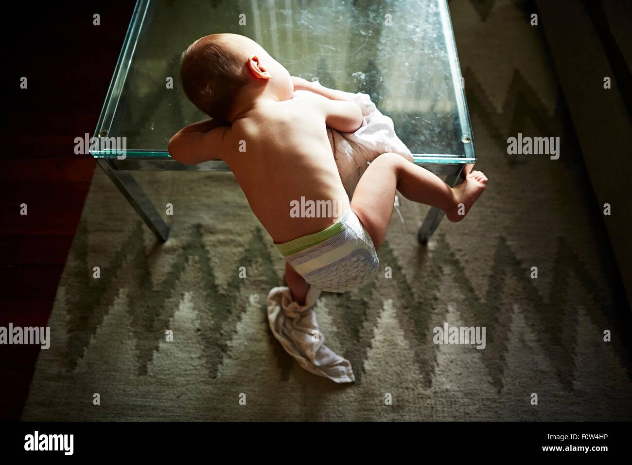 Boy half-climbing up on glass table Stock Photo