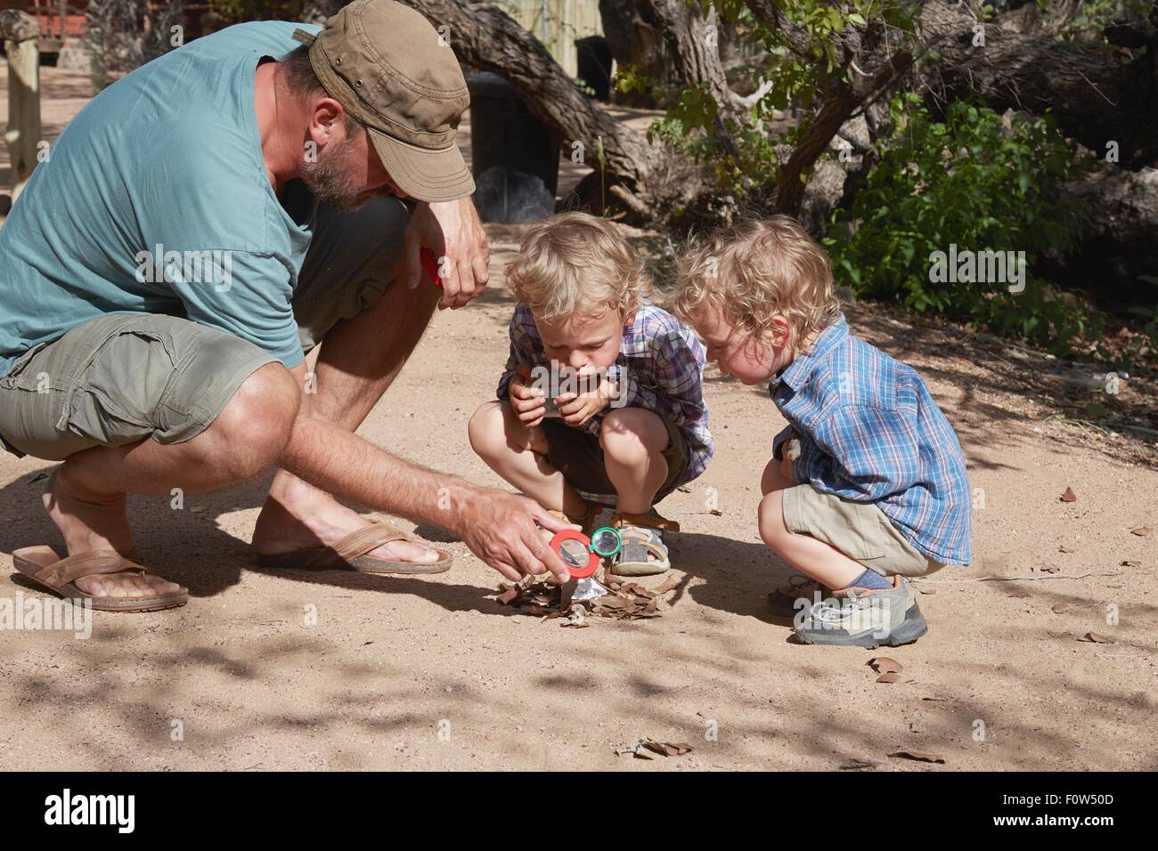 Father and sons trying to start camp fire using magnifying glass and sun, Purros, Kaokoland, Namibia Stock Photo