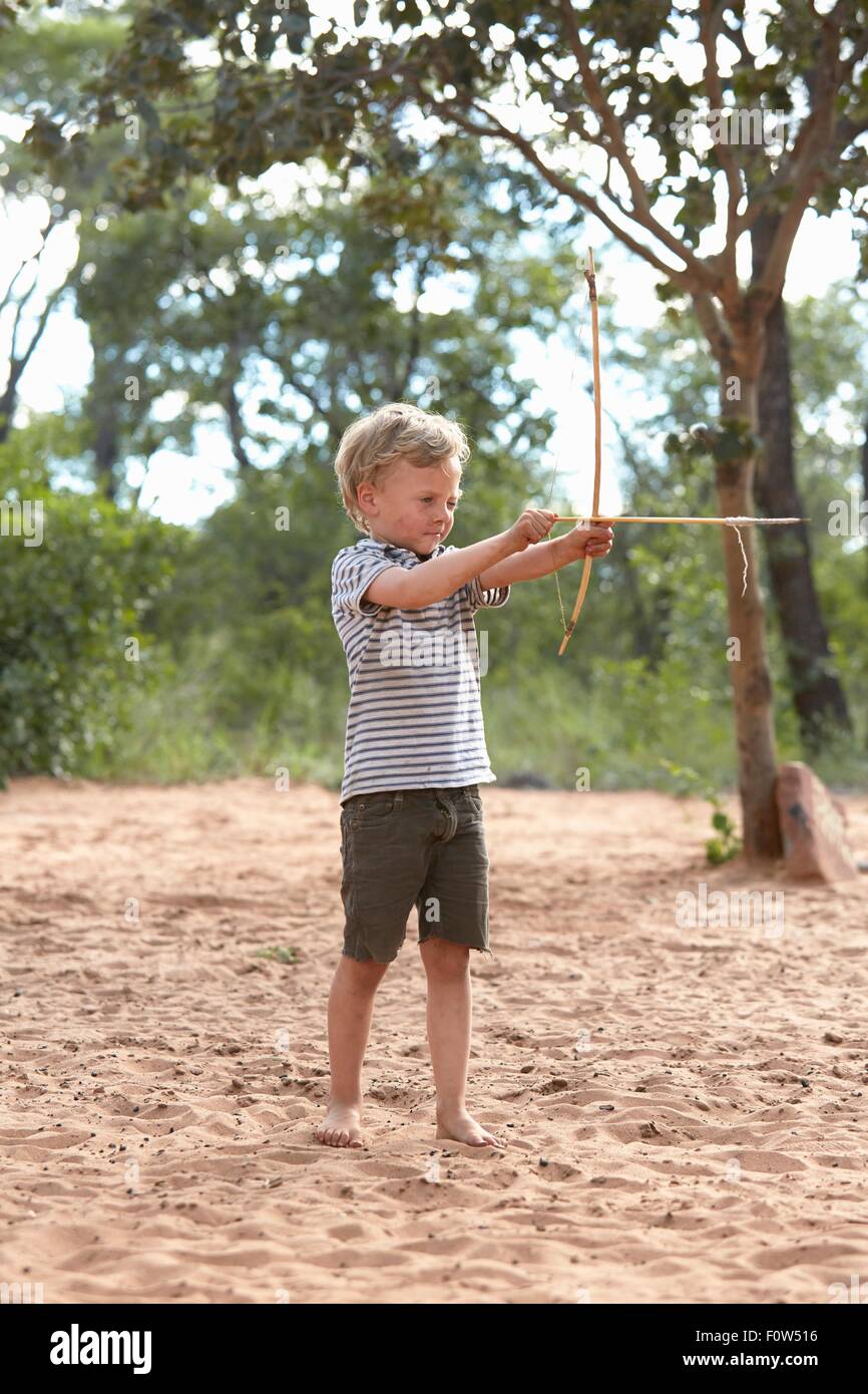 Young boy on sand holding home-made bow and arrow Stock Photo