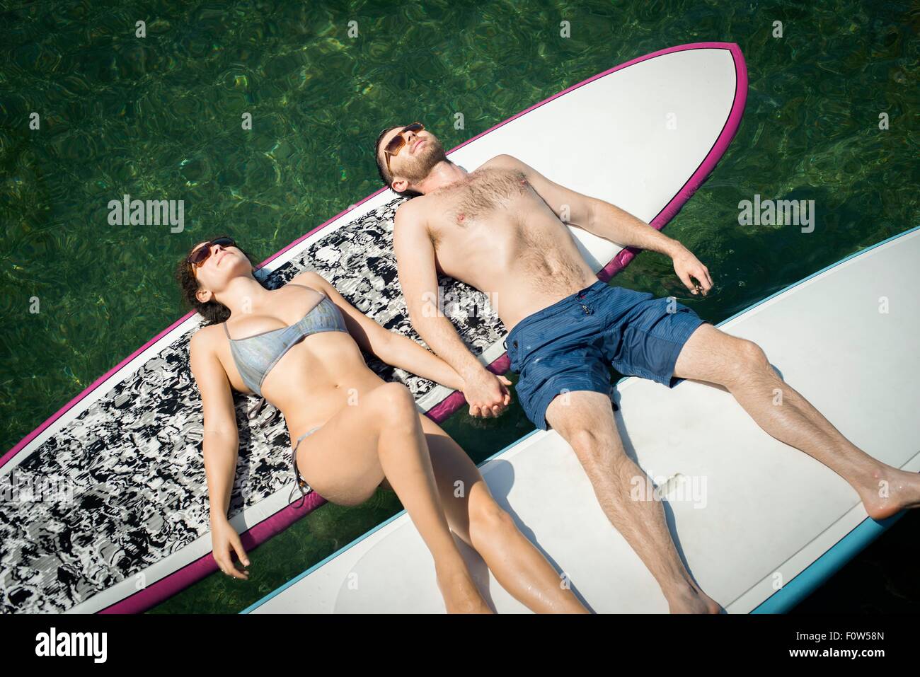 Overhead view of young couple sunbathing on paddleboards Stock Photo