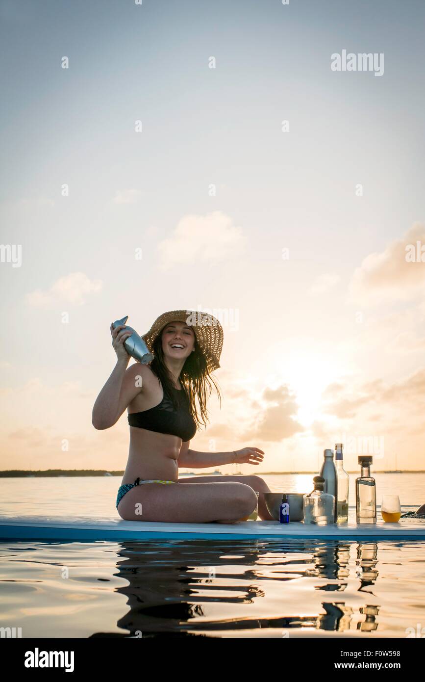 Young woman preparing cocktails on paddleboard at sunset, Islamorada, Florida, USA Stock Photo