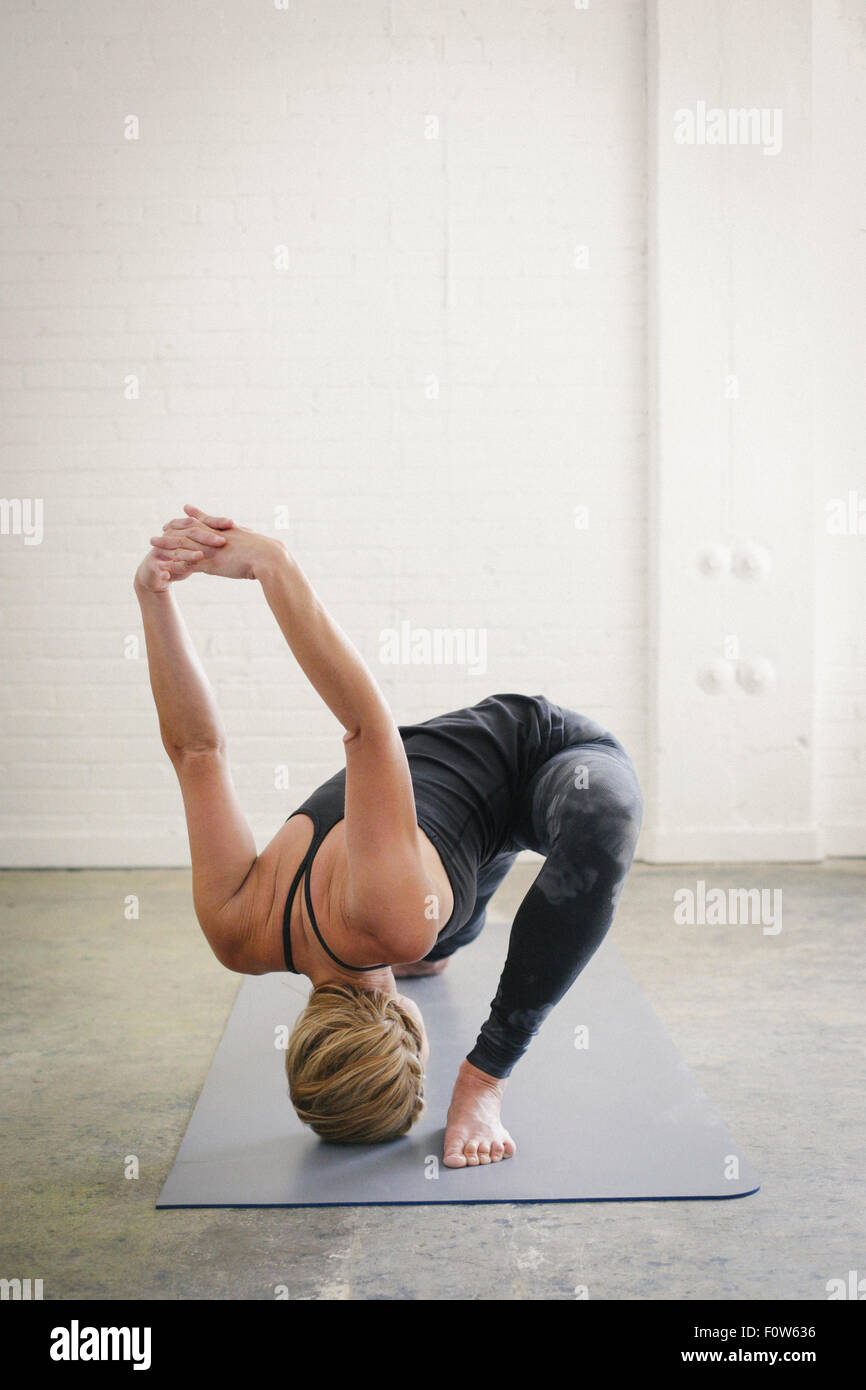 A blonde woman doing yoga, kneeling with her legs apart and her arms raised. Stock Photo
