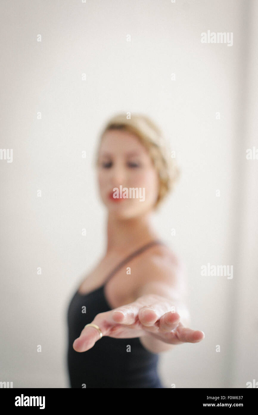 A blonde woman in a black leotard standing in a room, doing yoga, her arm outstretched. Stock Photo
