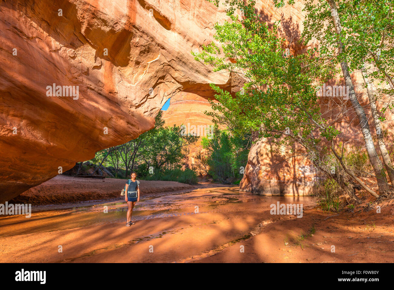 Girl Backpacker walking under Natural Bridge Arch Coyote Gulch Escalante National Stock Photo