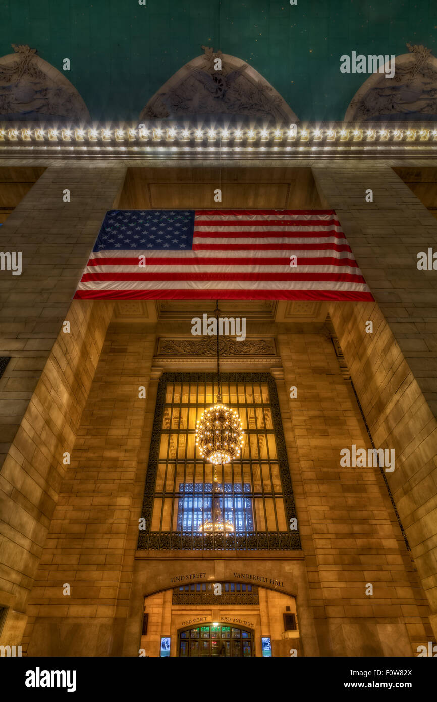 A view to the entrance to the main main concourse at Grand Central Terminal (GCT) in midtown Manhattan in New York City. This view shows the Beaux-Art style architecture, as well as the American Flag, the chandeliers and a piece of the celestial sky of the historic Grand Central Terminal. The terminal is more than a century old and is also referred to by many as the Grand Central Station. Stock Photo