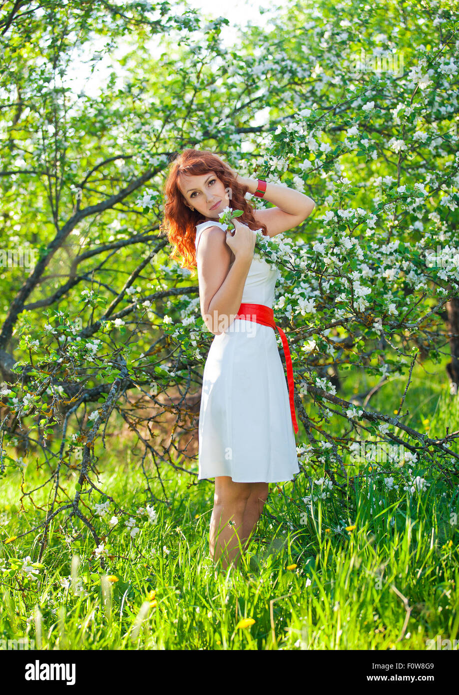 Free Happy Woman with Gorgeous Red Hair Enjoying Nature. Beauty Young Girl Outdoor in Spring Garden. Freedom concept. Healthy Smiling Girl over Green Flowers Nature Background. Apple-trees in Blossom Stock Photo