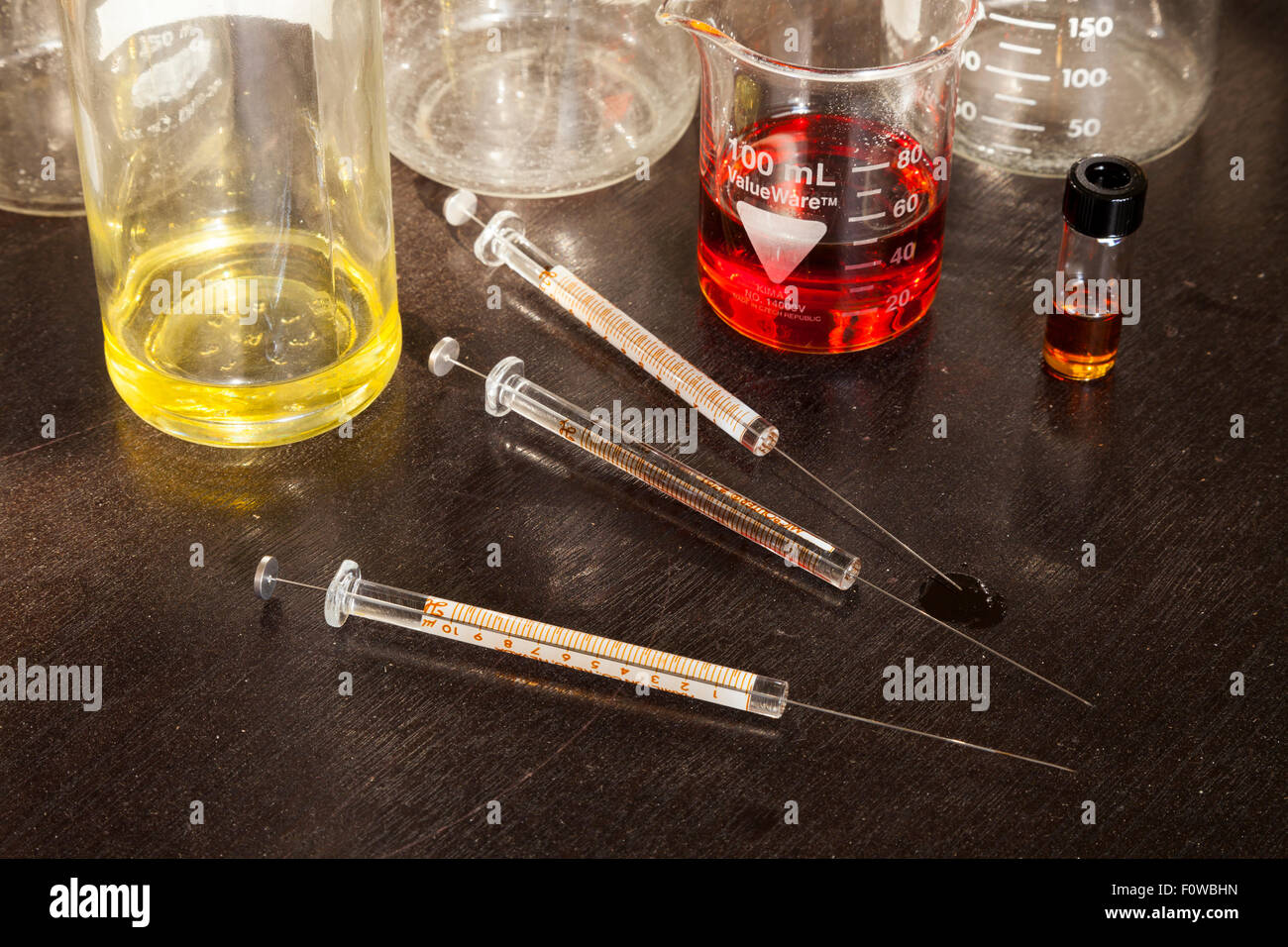 Beakers filled with coloured liquid and glass syringes sitting on a