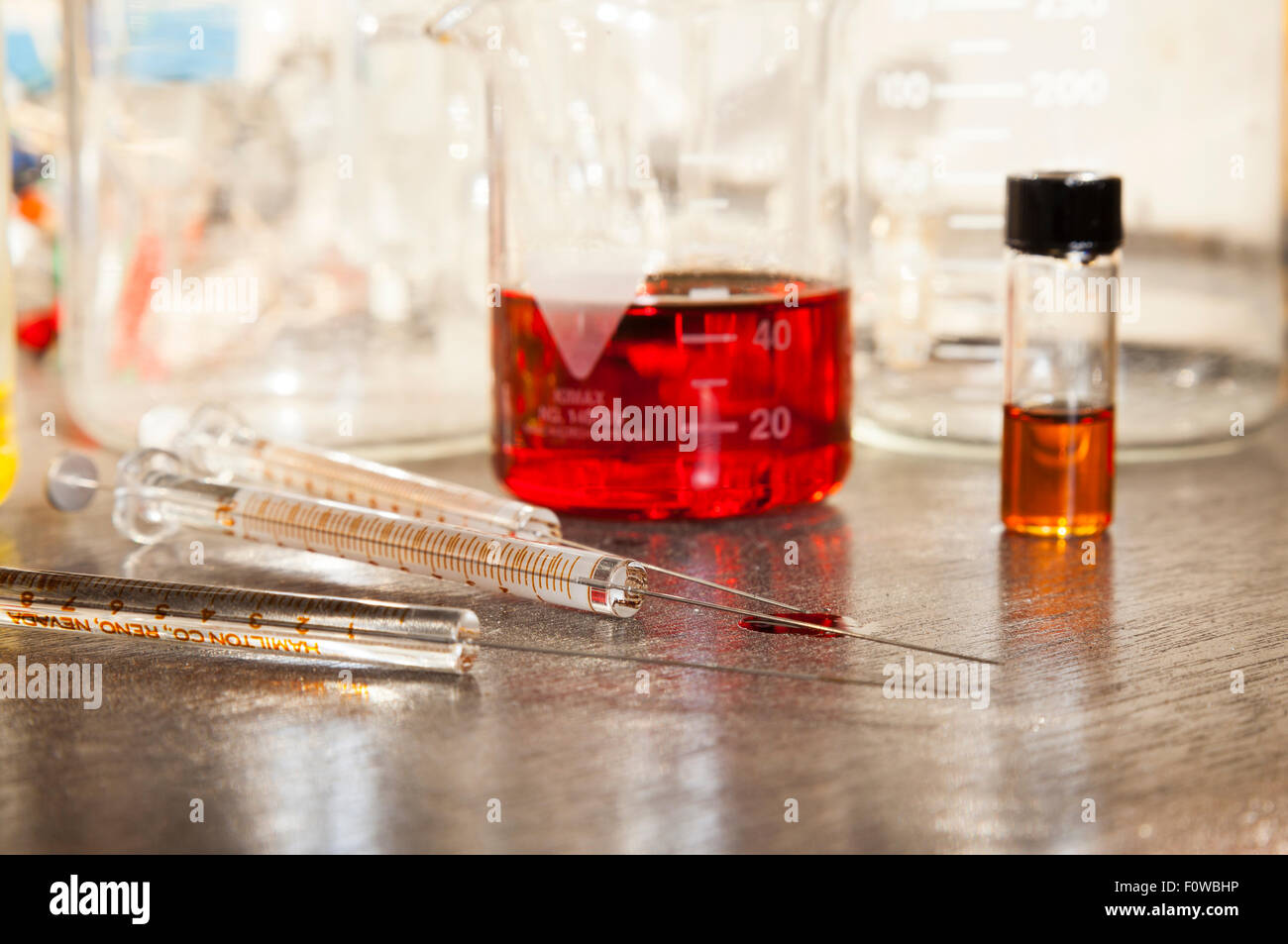 Beakers filled with coloured liquid and glass syringes sitting on a