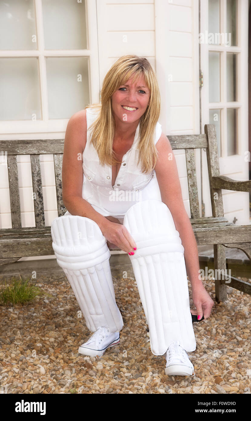 Woman putting on her cricket pads outside the pavilion before going in to bat in a ladies cricket match Stock Photo