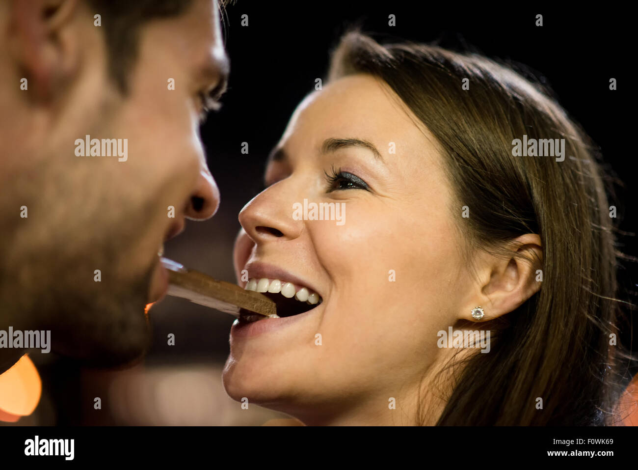Young couple eating together one piece of chocolate - in street at night Stock Photo