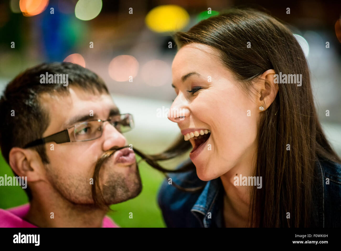 Couple having fun in street at night - man making moustache with his hair Stock Photo