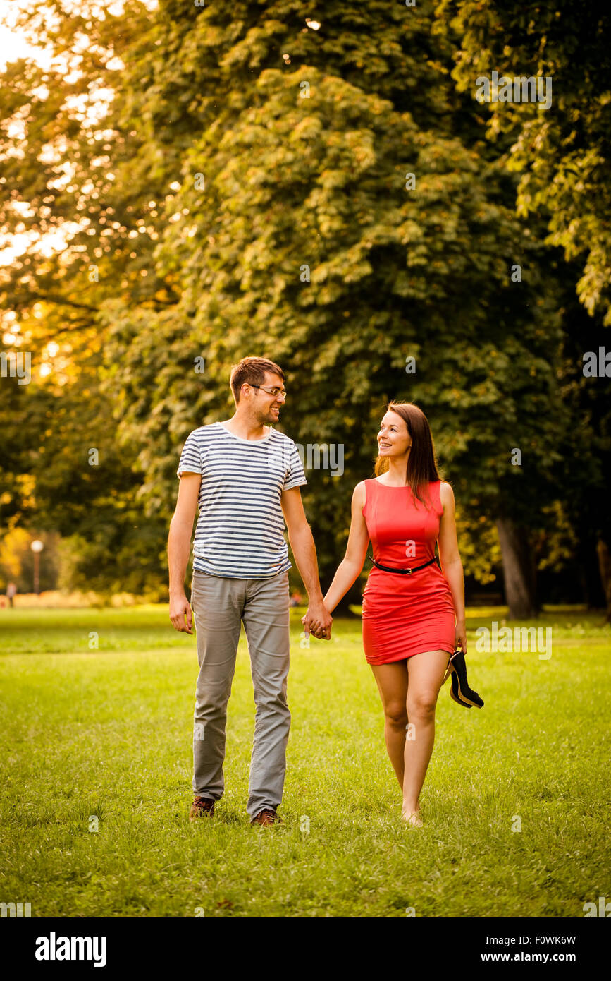 Couple walking in grass - woman is barefoot holding high heels shoes Stock Photo