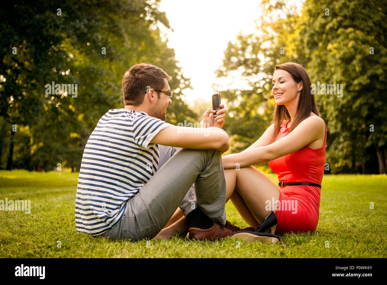 Young man taking photo of her girlfriend with mobile phone in nature Stock Photo