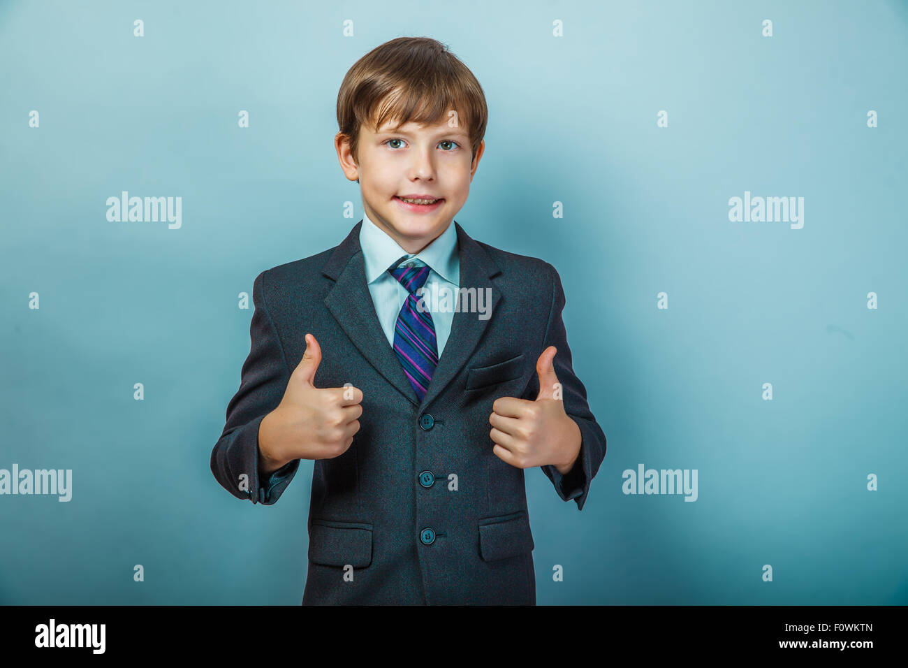Teen boy businessman in a suit showing gesture yes thumbs up on Stock Photo