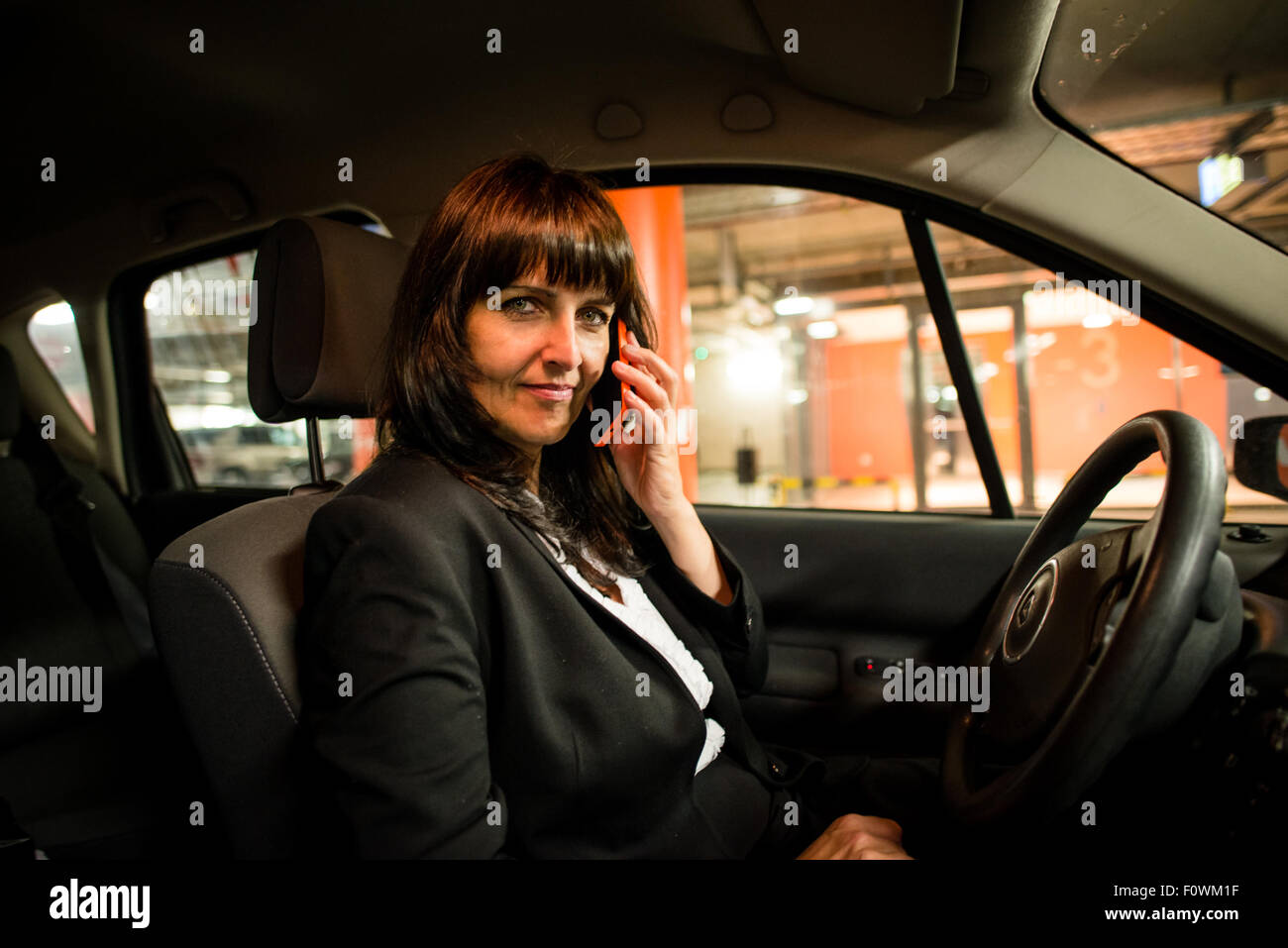 Senior business woman calling mobile phone in car - night scene, looking to camera Stock Photo