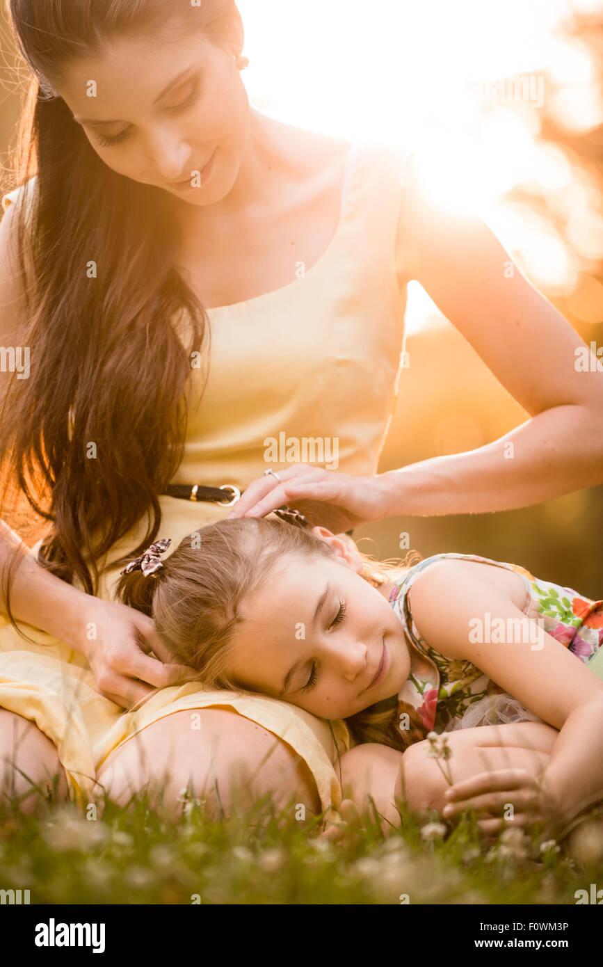 Mother is caressing her child resting on knees outdoor in nature Stock Photo