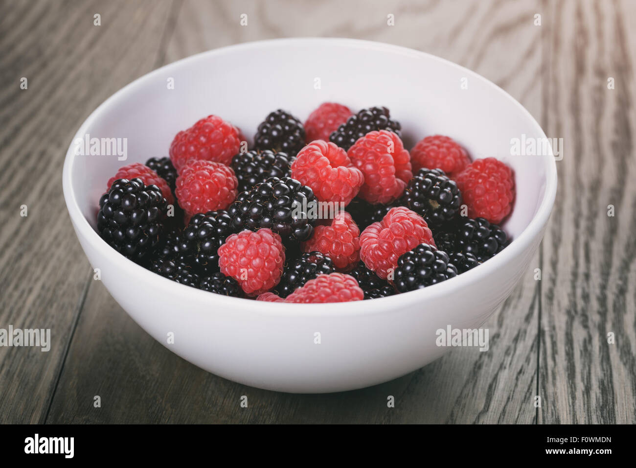 raspberries and blackberries in white bowl on wood table Stock Photo