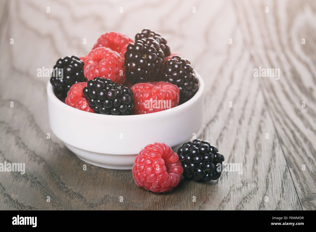 raspberries and blackberries in white bowl on wood table Stock Photo