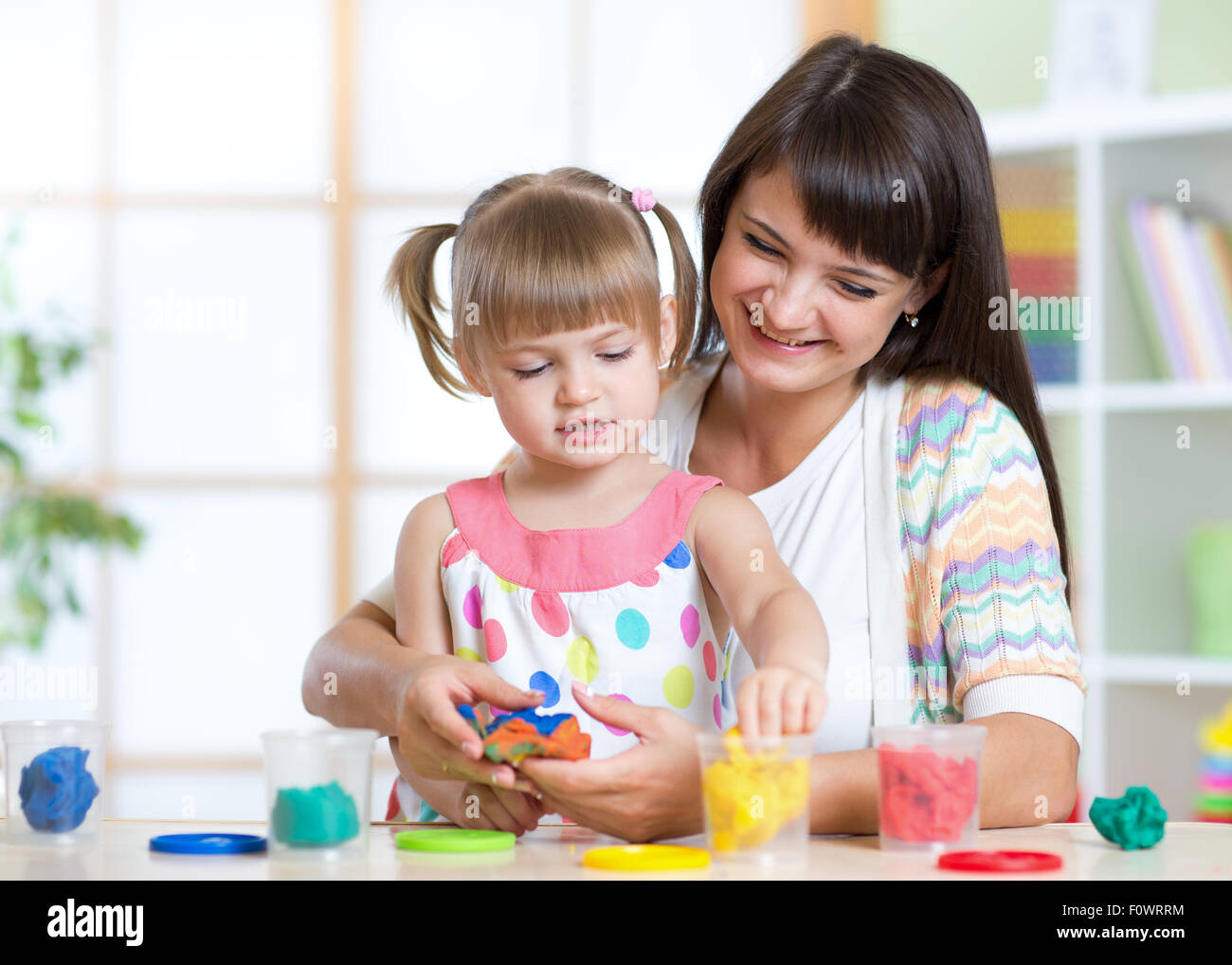 Happy child and mother sitting at table and playing with colorful clay toy Stock Photo