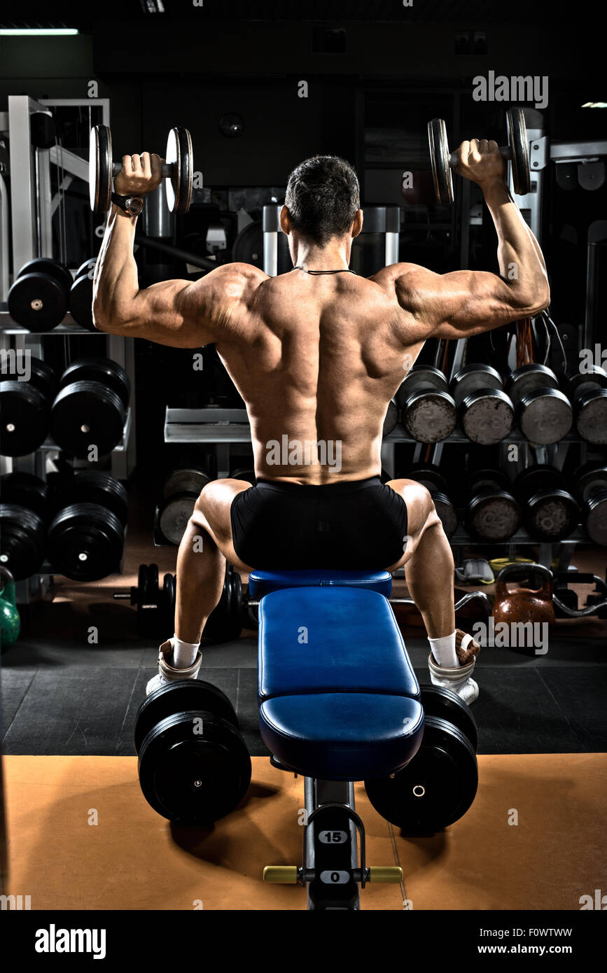 very brawny guy bodybuilder,  execute exercise with  dumbbells, on deltoid muscle shoulder Stock Photo
