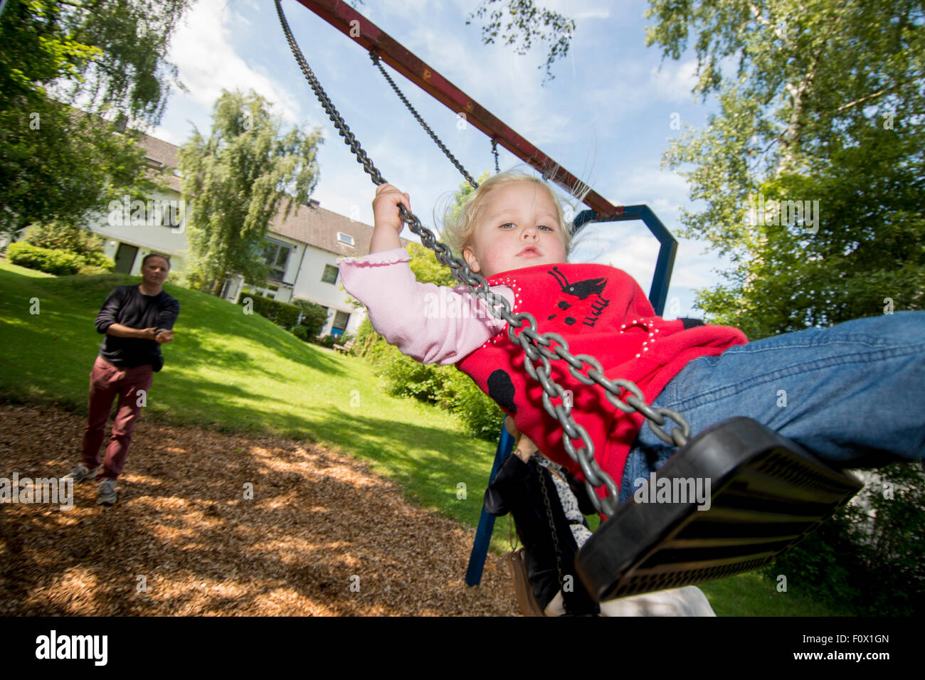 Little girl on swing with Dad in background. Stock Photo