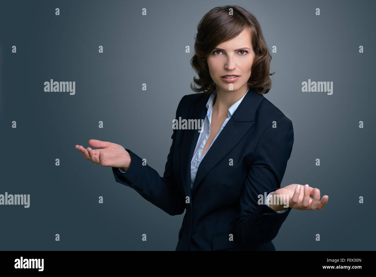 Half Body Shot of a Confused Young Businesswoman with Hands in the Air, Looking into the Distance Against Gray Wall. Stock Photo