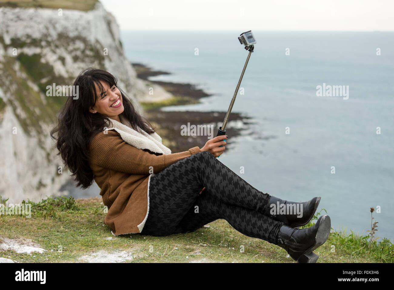 Young woman taking a selfie with a GoPro camera and a selfie stick. The White Cliffs of Dover, Dover, Kent, UK Stock Photo