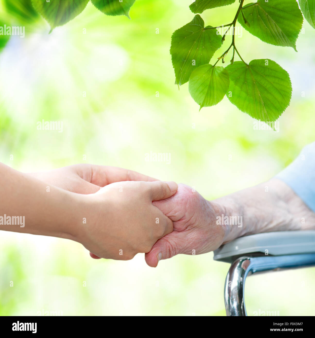 Elderly woman in wheel chair holding hands with young caretaker Stock Photo