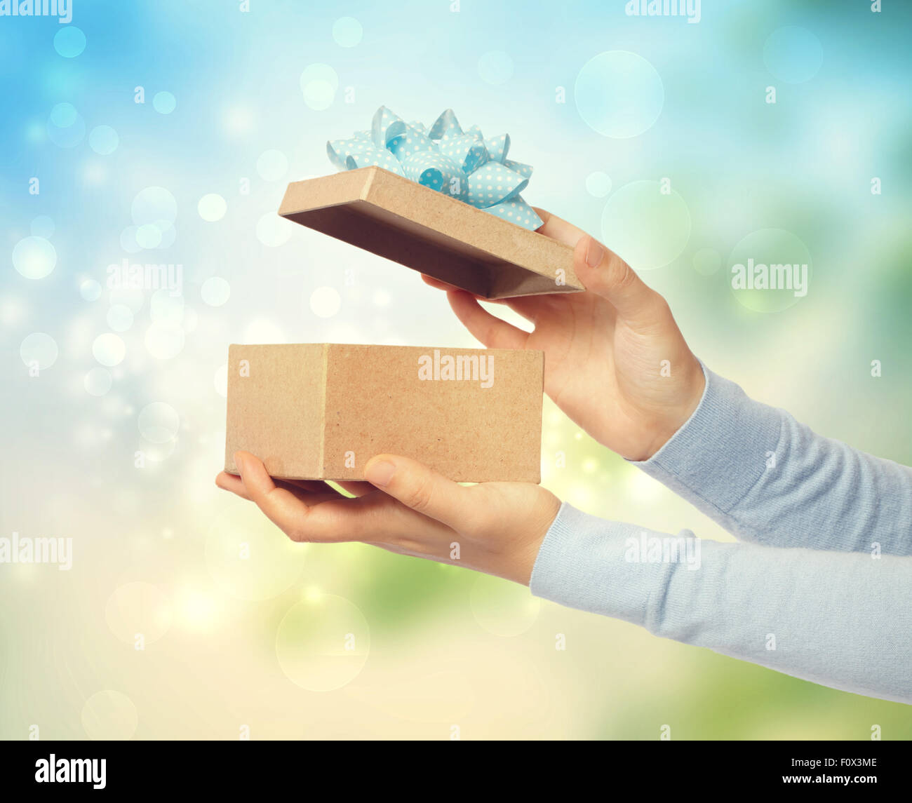 Woman opening and presenting gift box on bright background Stock Photo