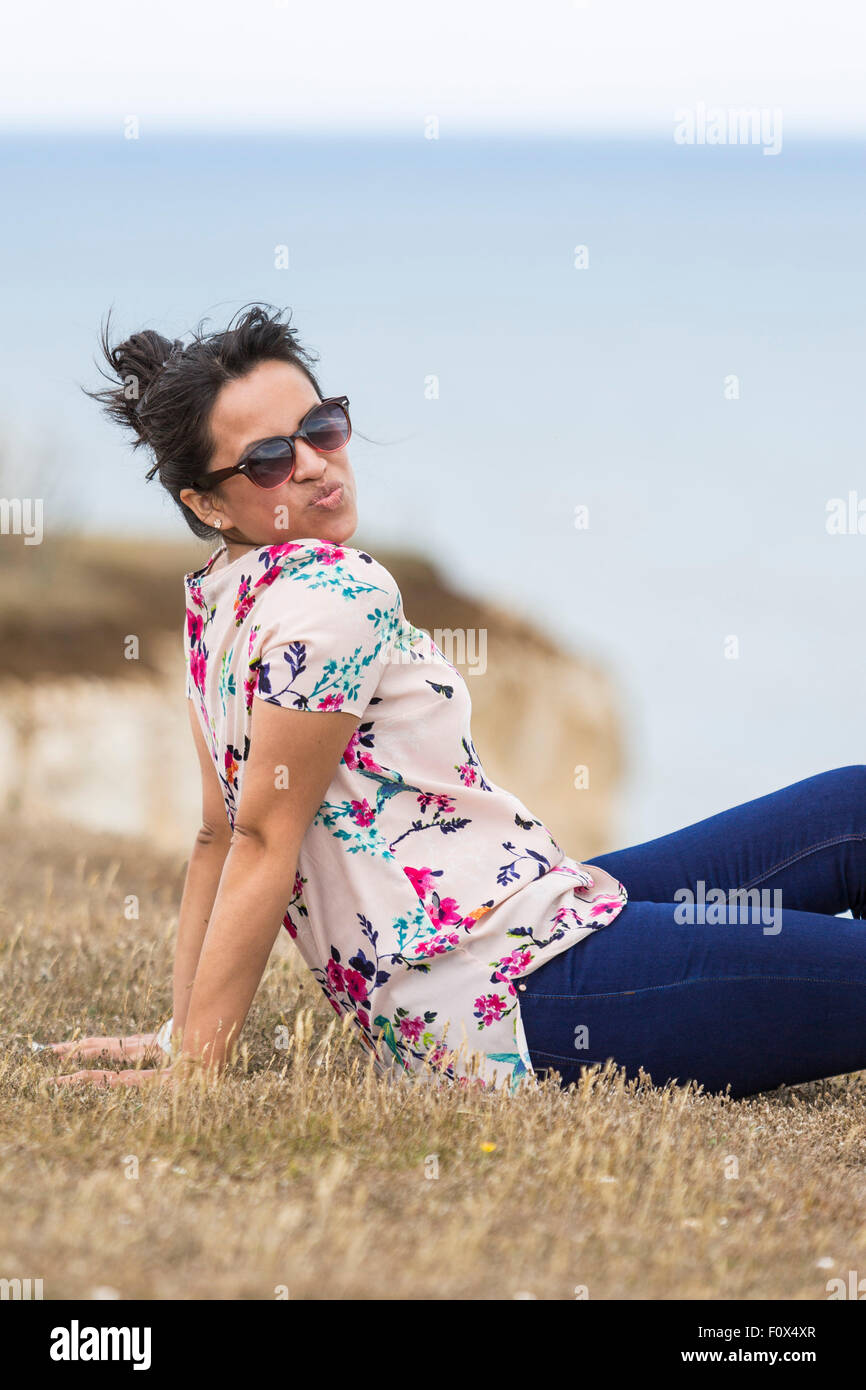 Young woman wearing sunglasses and sitting on the grass. The Seven Sisters Cliffs, South Down National Park, East Sussex, UK Stock Photo