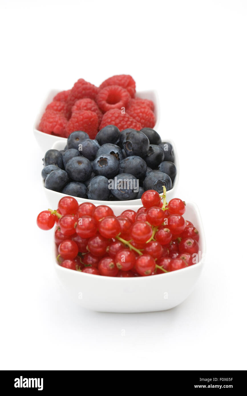 Redcurrants, Blueberries and Raspberries in white bowls on a white background. Stock Photo