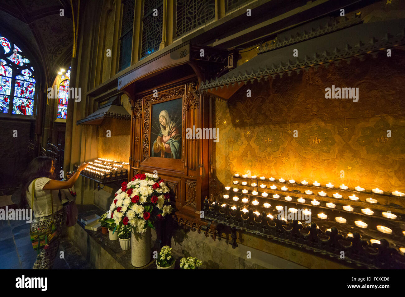 Devotion in the Aachen cathedral, woman lighting a candle with a painting of the virgin Mary, Germany Stock Photo