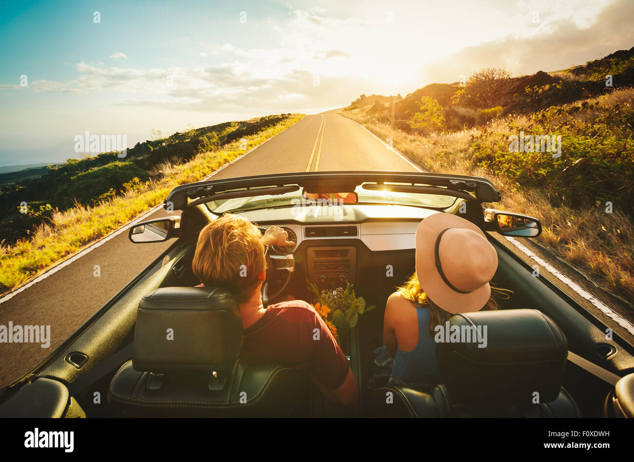 Happy Young Couple Driving Along Country Road in Convertible at Sunset Stock Photo