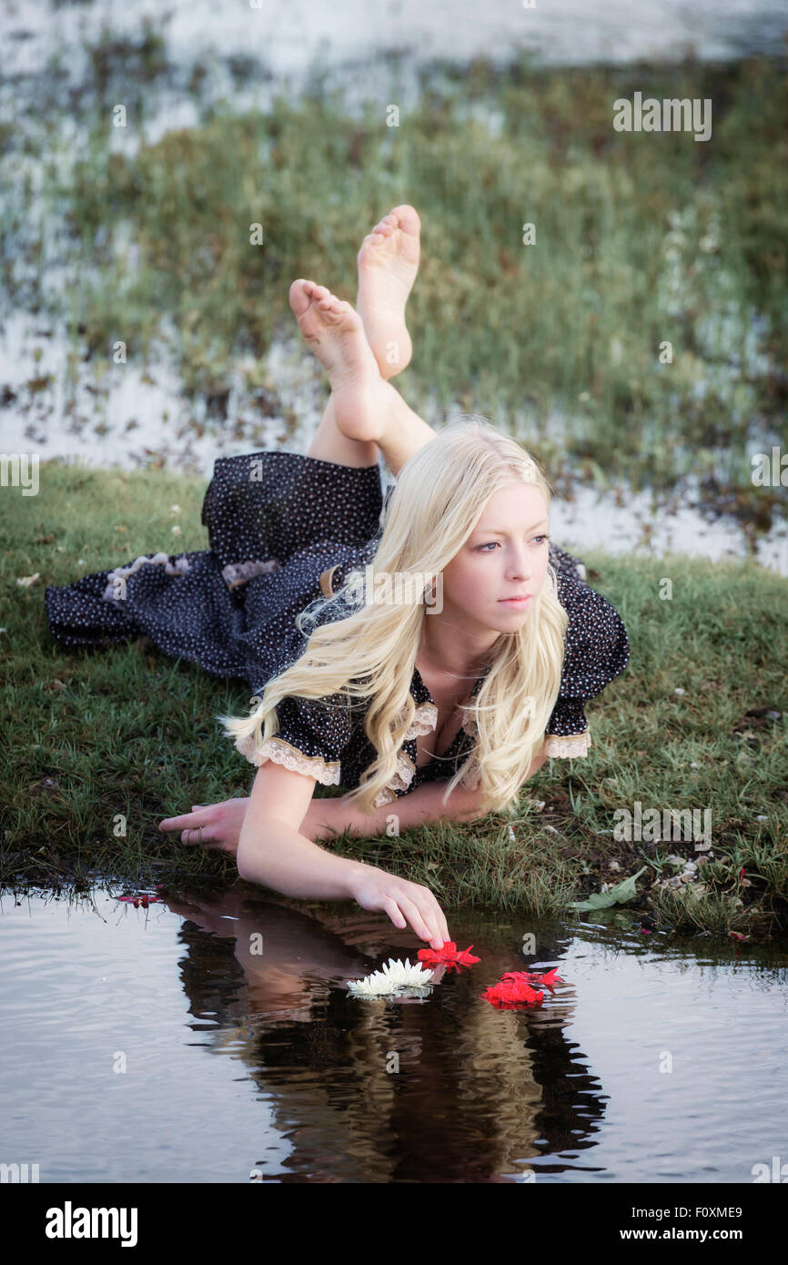 a blond girl is placing flowers on a pond Stock Photo