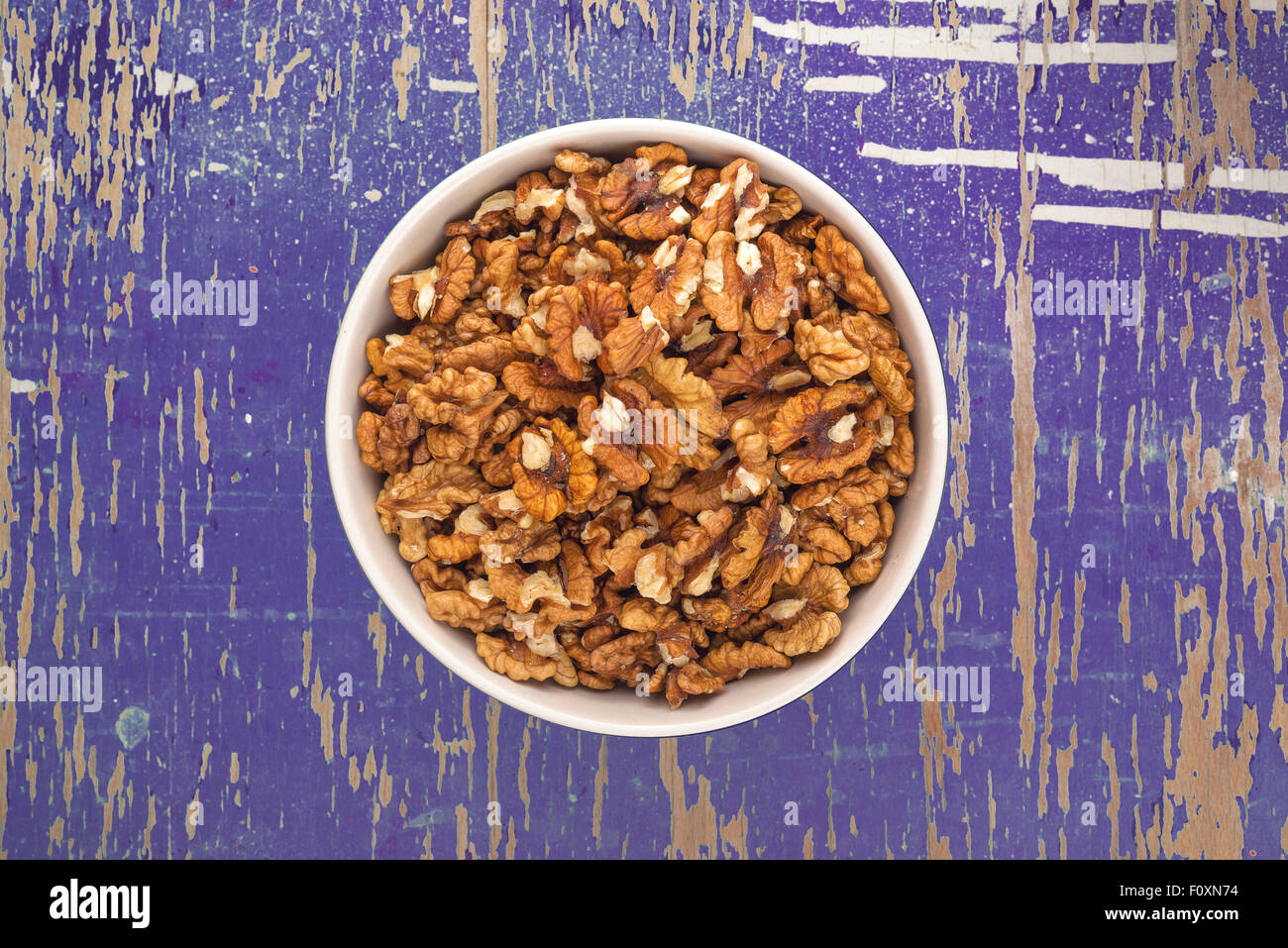 Peeled Walnut Kernels in Ceramic Bowl on Purple Rustic Wood Plank Background, Top View Stock Photo