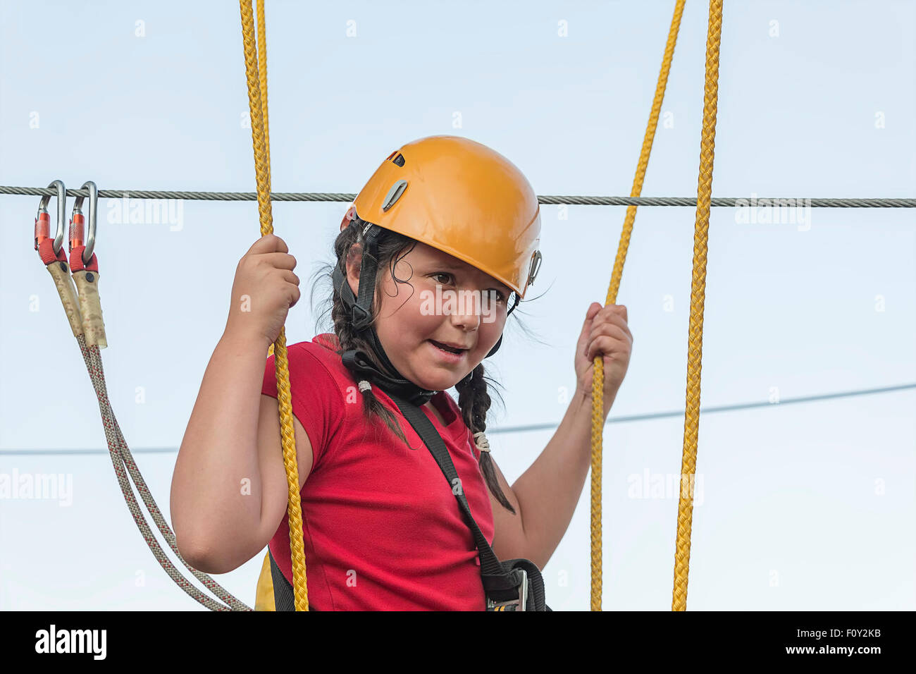 Child girl climbing in adventure park, expressing strong emotion. Stock Photo