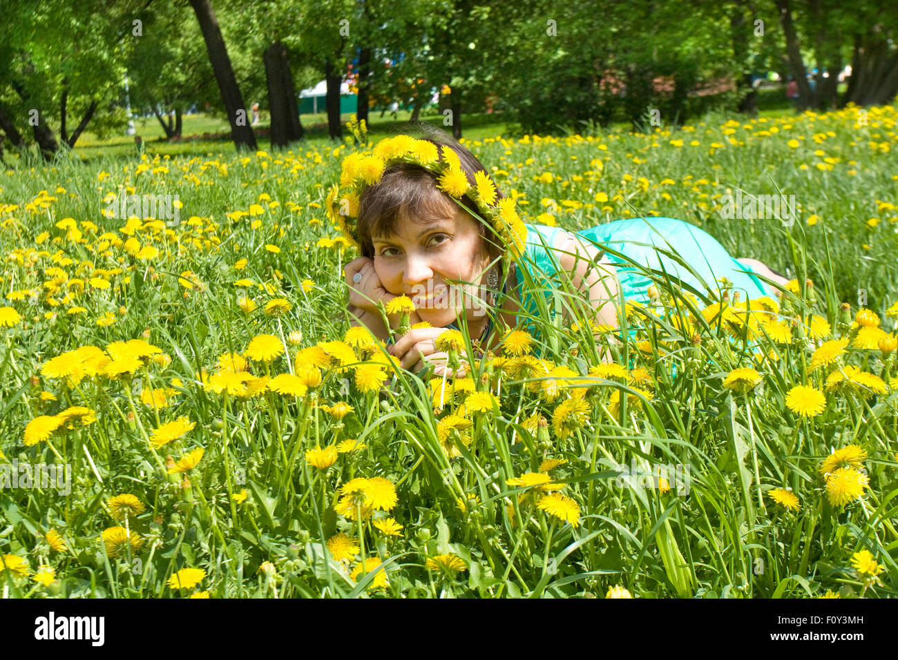 European lady brunette in wreath of yellow dandelions laying on meadow with dandelions. Stock Photo