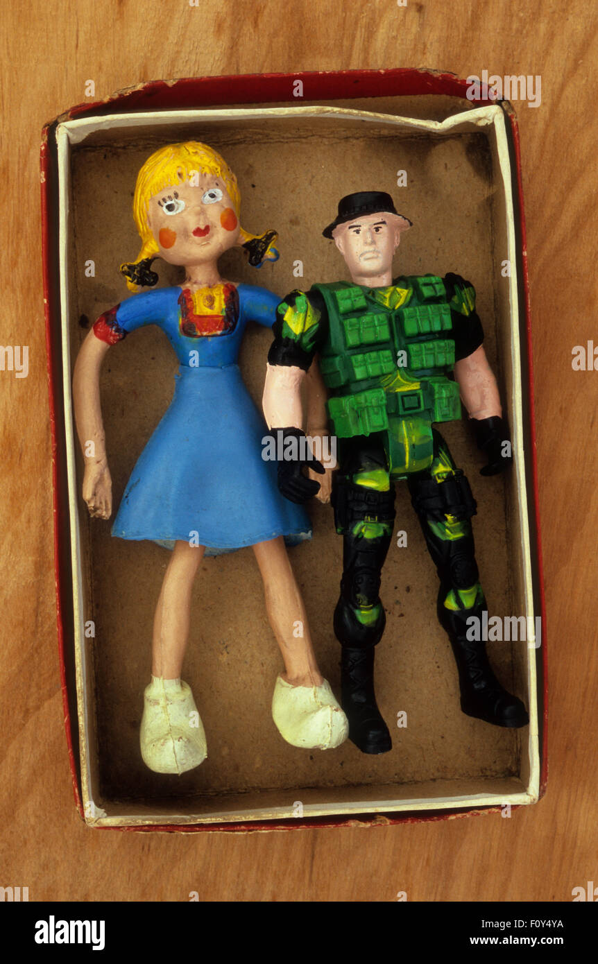 Bendy rubber girl doll with blue dress standing in box next to action man commando with ammunition waistcoat Stock Photo