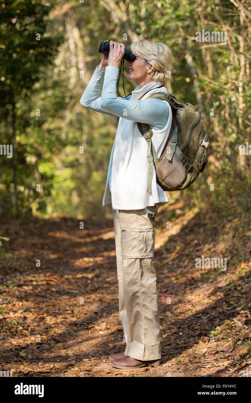 side view of mid age woman using binoculars bird watching in forest ...