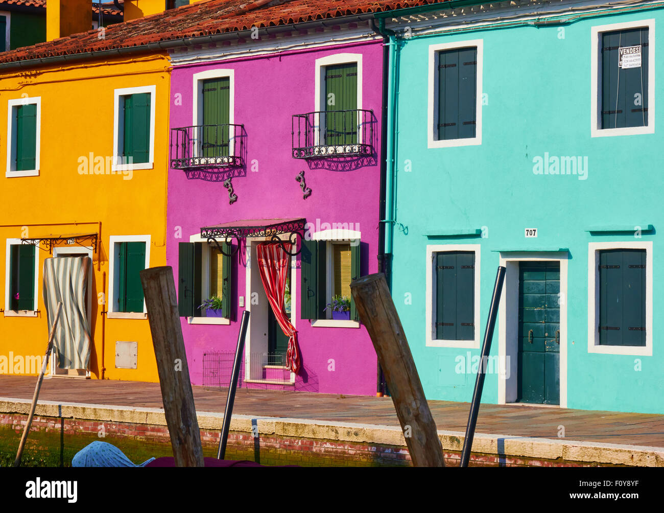 Colourful row of canalside houses and wooden mooring poles Burano